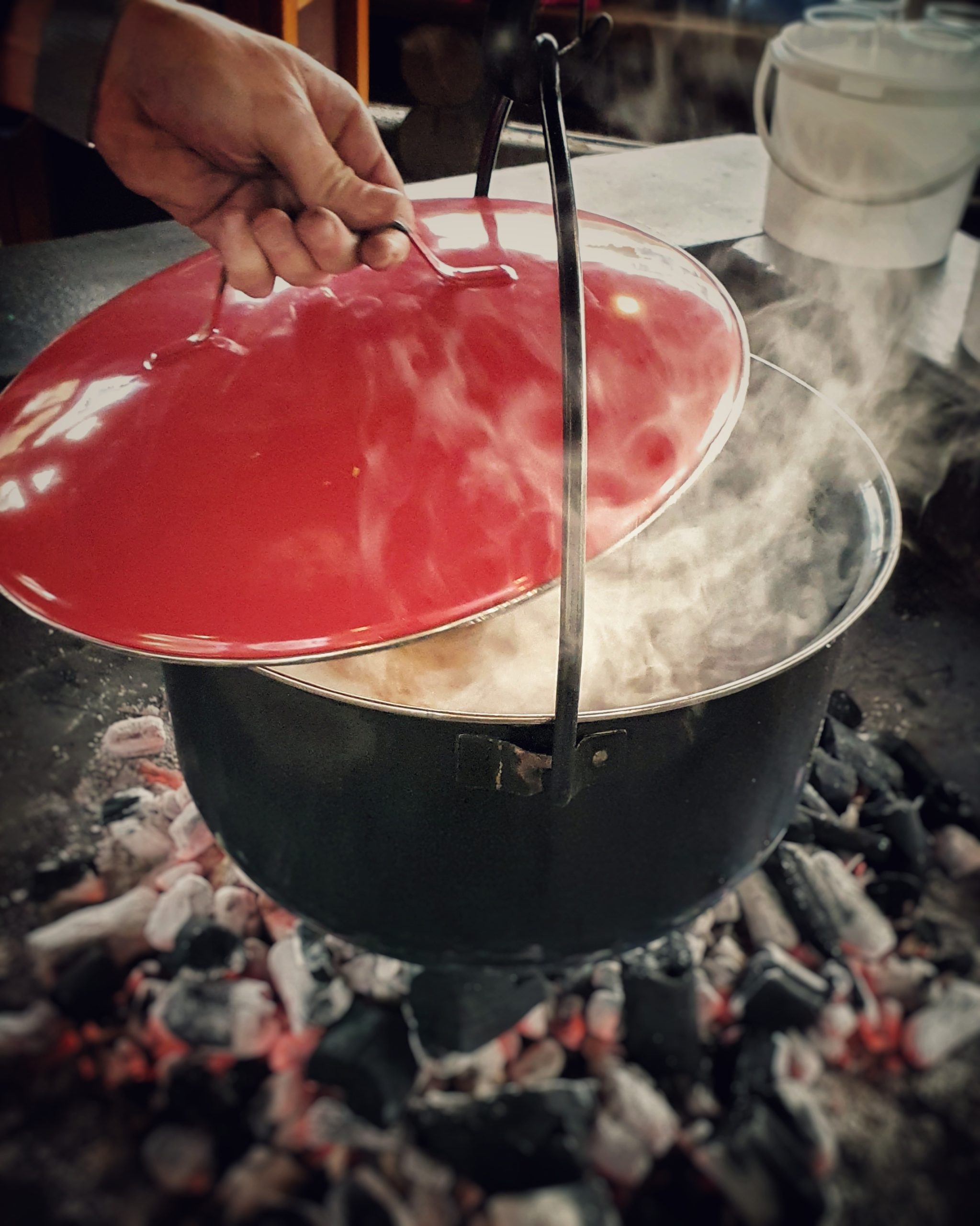 Kochtopf mit rotem Deckel über heiße Glut